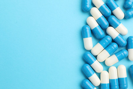 Pills on light blue background, flat lay. Space for text