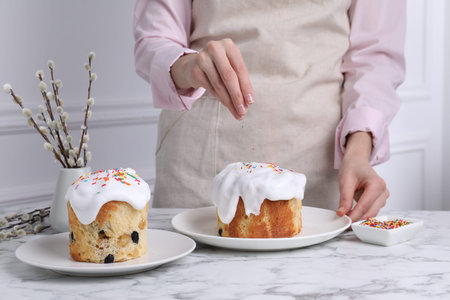 Woman decorating Easter cake with colorful sprinkles at white marble table indoors, closeup