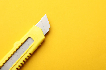 One sharp paper knife on yellow background, closeup. Space for text