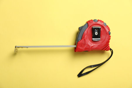 Measuring tape on yellow background, top view