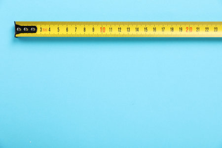 Measuring tape on light blue background, top view. Space for text