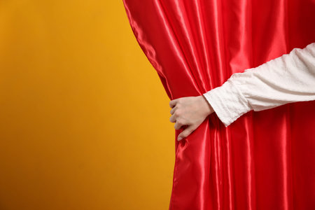Woman opening red front curtains on orange background, closeup. Space for text