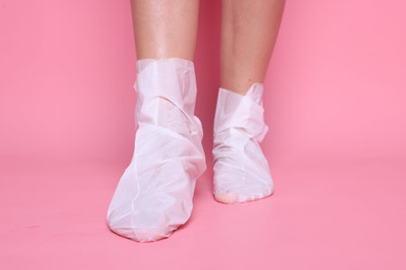 Woman wearing disposable moisturizing socks on her feet against pink background, closeupの写真素材