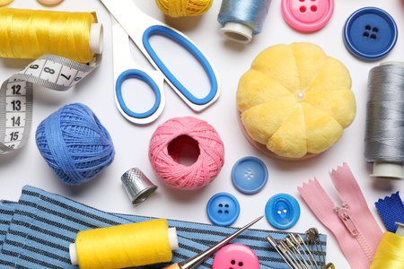 Different sewing supplies on white background, flat lay