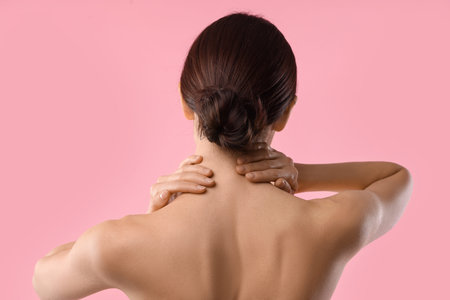 Beautiful woman touching her neck on pink background, back viewの写真素材