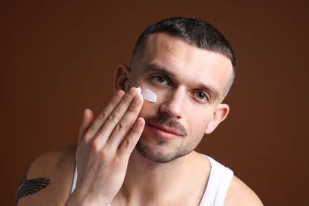 Man applying cream onto his face against brown backgroundの写真素材