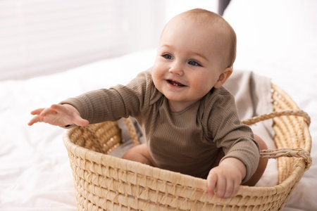 Cute little baby in wicker basket on bed at homeの写真素材