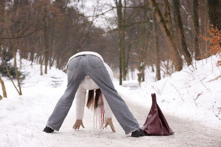 Young woman falling on slippery pathway covered in ice outdoors, back view