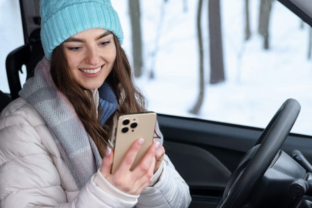 Woman with smartphone in car at snowy forest