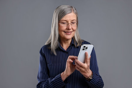 Beautiful senior woman with smartphone on gray background
