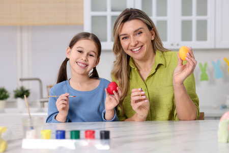 Easter celebration. Mother and her daughter painting eggs at white marble table in kitchen
