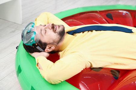 Office worker with diving mask on inflatable mattress indoors