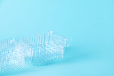 Plastic packaging. Stack of disposable containers on light blue background, closeup. Space for text