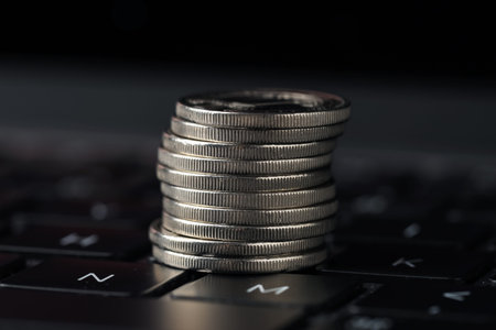 Stack of coins on laptop against dark background, closeup