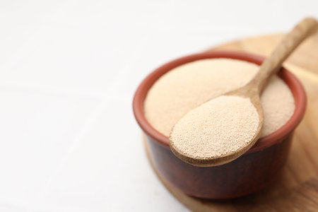 Dry yeast in bowl and spoon on white table, closeup. Space for textの写真素材