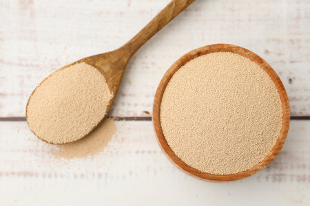 Dry yeast in bowl and spoon on white wooden table, top viewの写真素材