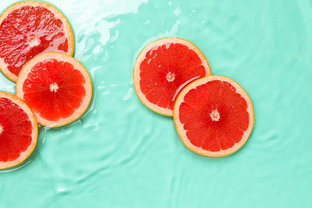 Slices of grapefruit in water on turquoise background, flat layの写真素材
