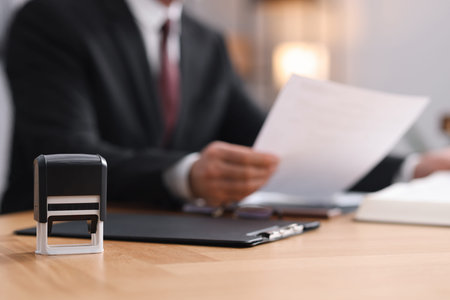 Notary in suit doing paperwork at wooden table in office, focus on stamp and clipboard