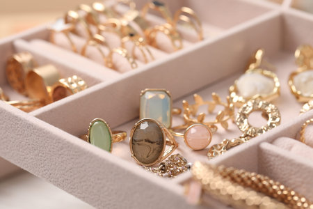 Beige tray with different gold jewelry against blurred background, selective focus