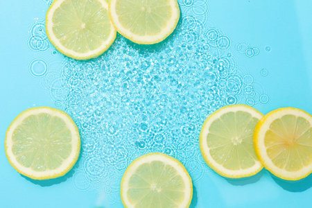 Lemon slices in water on light blue background, flat lay. Space for textの写真素材