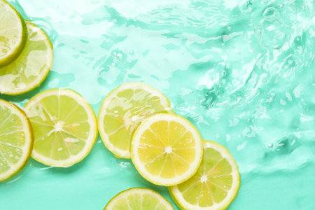 Slices of citrus fruits in water on turquoise background, flat lay. Space for textの写真素材
