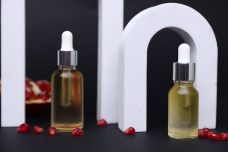 Bottles of essential oil and pomegranate seeds on dark background, closeup