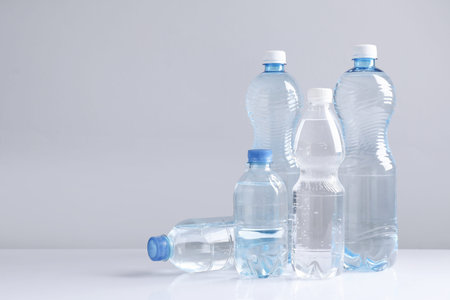 Water bottles of different sizes on white table against gray background, space for text