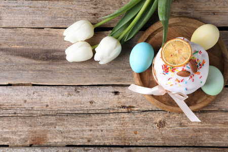 Delicious Easter cake, tulips and painted eggs on wooden table, flat lay. Space for text