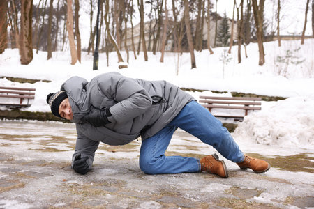 Young man fallen on slippery pathway covered in ice outdoorsの写真素材