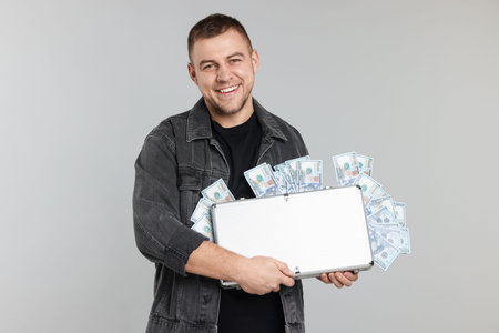 Happy man with briefcase full of money on light gray backgroundの写真素材