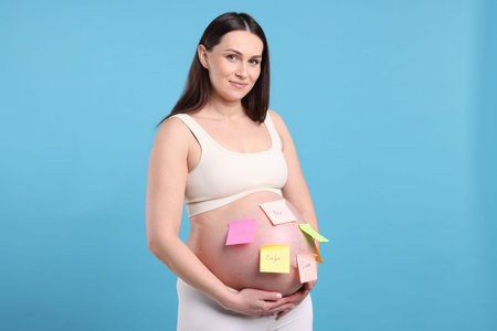 Pregnant woman with notes with different names on her belly against light blue backgroundの写真素材