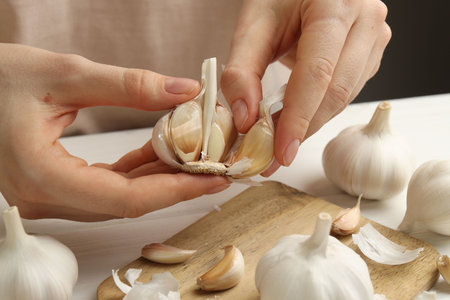 Woman peeling fresh garlic at white wooden table, closeupの写真素材