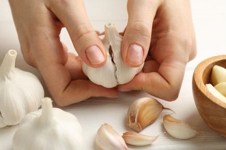Woman peeling fresh garlic at white wooden table, closeupの写真素材