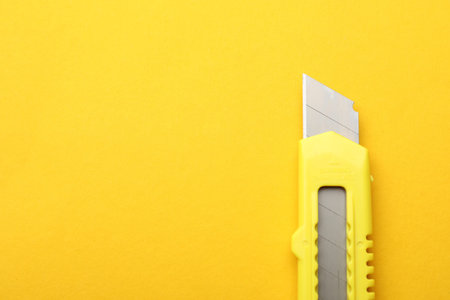 One sharp paper knife on yellow background, top view. Space for text
