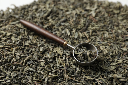 Measuring spoon on dried green tea leaves, closeup