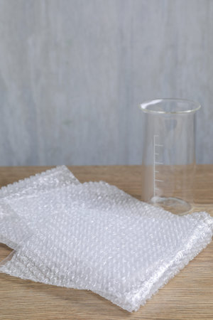 Bubble wrap and glass beaker on wooden table, closeup