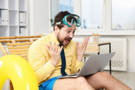 Office worker with diving mask and laptop in deck chair indoors