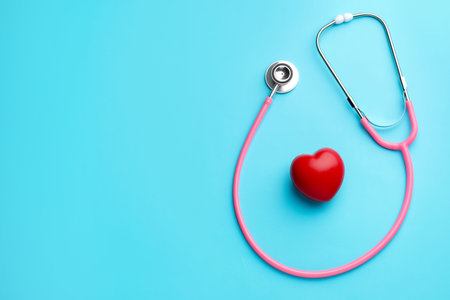 Pink stethoscope and heart model on light blue background, top view. Space for text