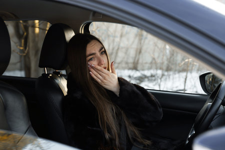 Young woman feeling fatigue in her modern car, view from outsideの写真素材