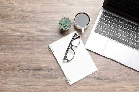 Modern laptop, coffee, notebook, glasses and plant on wooden table, flat lay. Space for textの写真素材