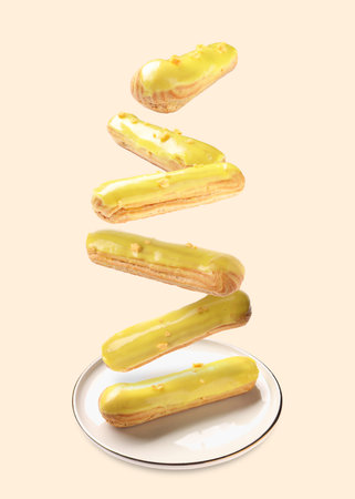 Eclairs with glaze falling onto plate against beige background