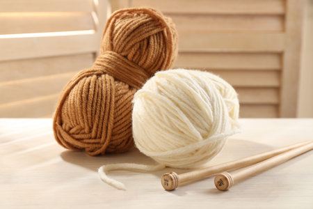 Knitting yarns and needles on white wooden table indoors, closeup
