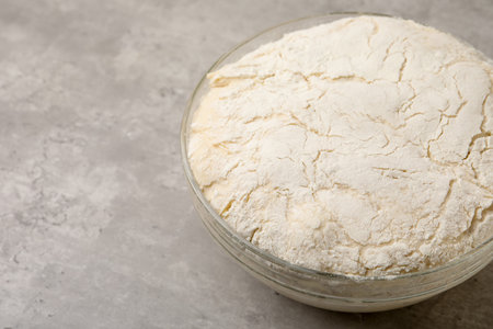 Fresh yeast dough in glass bowl on gray textured table, closeup. Space for text