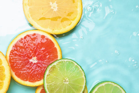 Slices of citrus fruits in water on turquoise background, flat lay