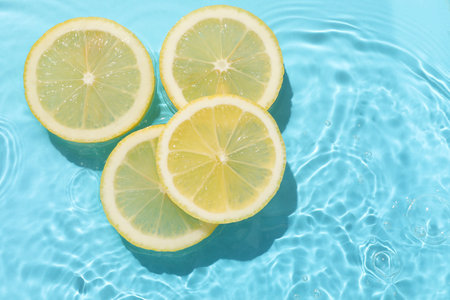 Lemon slices in water on light blue background, flat lay. Space for text