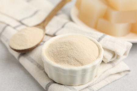 Powder in bowl, spoon and jelly cubes on gray table, closeup