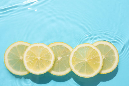Lemon slices in water on light blue background, flat lay. Space for textの写真素材