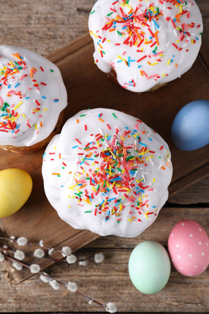 Delicious Easter cakes, painted eggs and willow branches on wooden table, flat lay