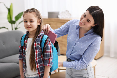 Mother helping her daughter to pack backpack for school at homeの写真素材
