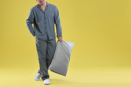Man in stylish pajamas with pillow on yellow background, closeup. Space for text